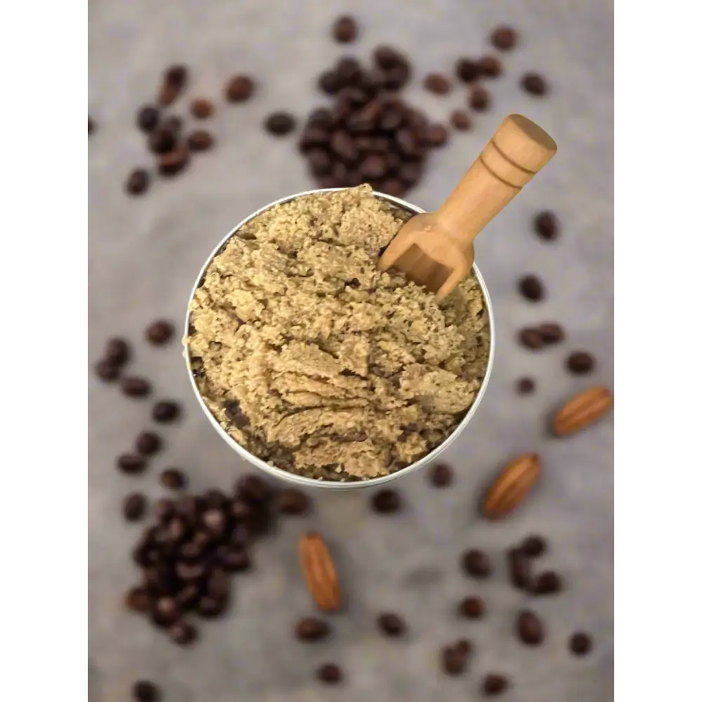A metallic measuring cup with coarse brown coffee grounds and wooden scoop for organic coconut coffee scrubs
