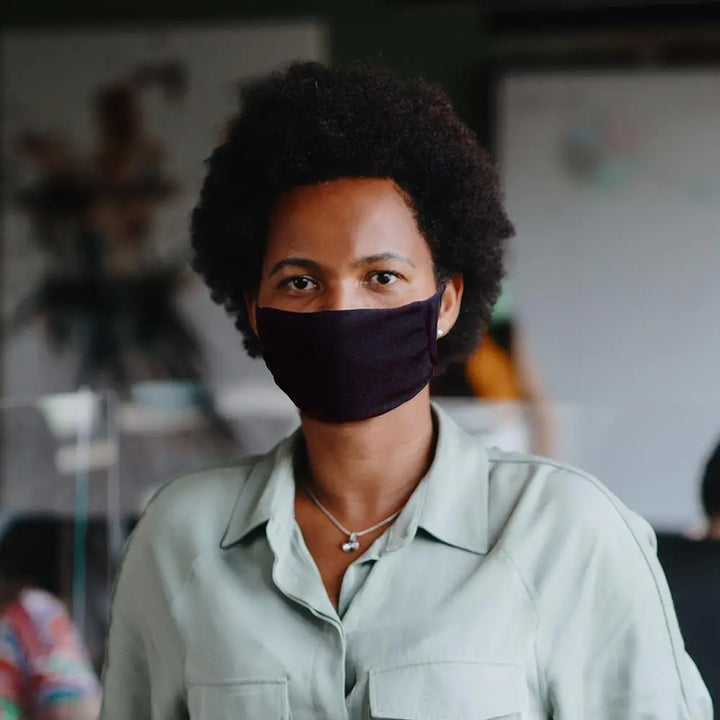 A woman with dark curly hair wearing a black breathable smart temp face mask for all-day protective comfort