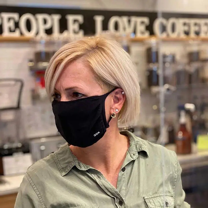 Blonde woman wearing breathable smart temp protective face mask in black with 30xmask ear loop and olive green shirt