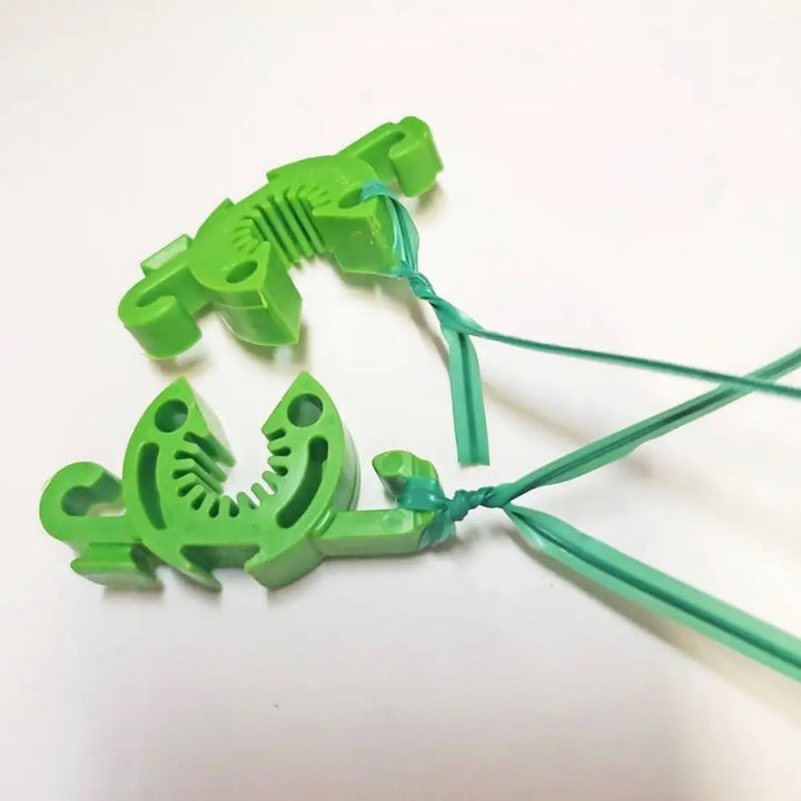 Bright green plastic dinosaur-shaped modular plant support clip with teal string for customizable tomato cage connectors