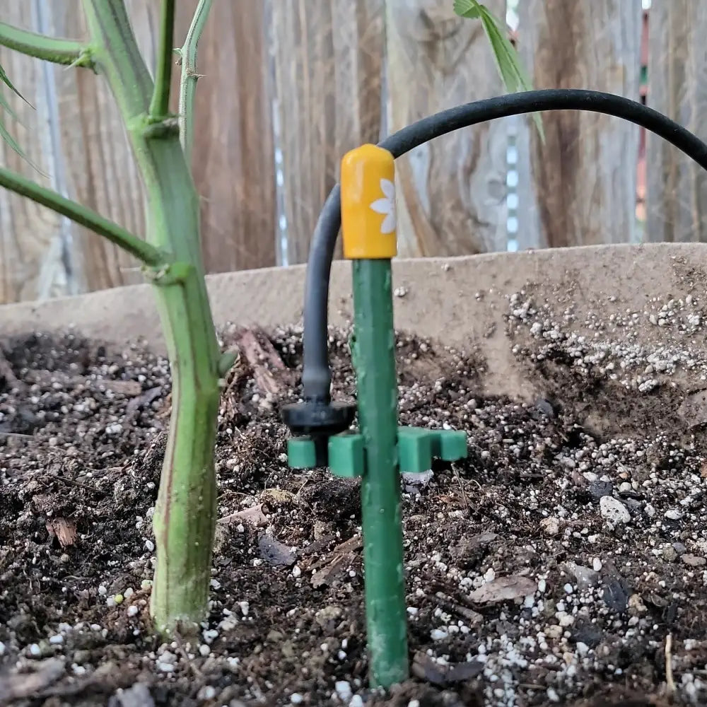Green plastic drip irrigation emitter with yellow cap and white flower design for modular plant support clips