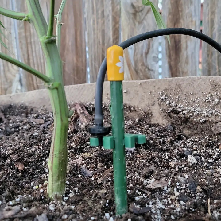 Green plastic drip irrigation emitter with yellow cap and white flower design for modular plant support clips