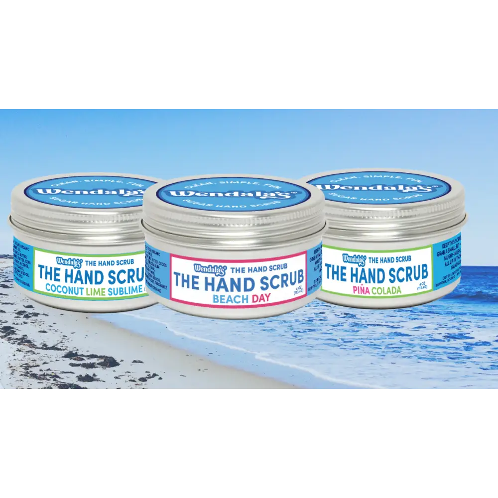Three cylindrical metal jars of wendala’s®️ hand scrubs in coconut lime sublime green beach day pink and piña colada blue with white lids in coastal hand scrub bundle