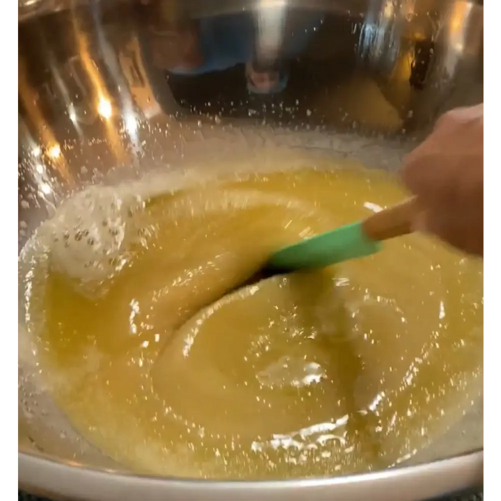 A green silicone spatula with wooden handle stirring a yellow mixture in a bowl for wendalas crab rosemary mint organic coconut product