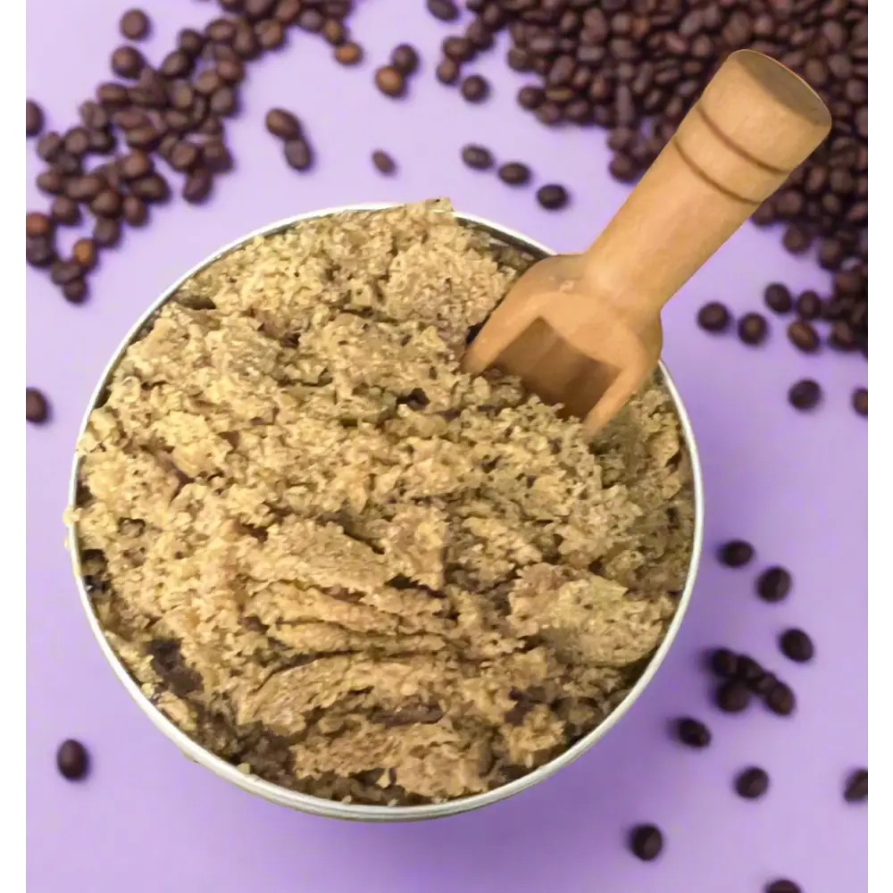 A rustic wooden scoop in a metallic bowl filled with brown sugar coffee scrub for organic coconut foot care