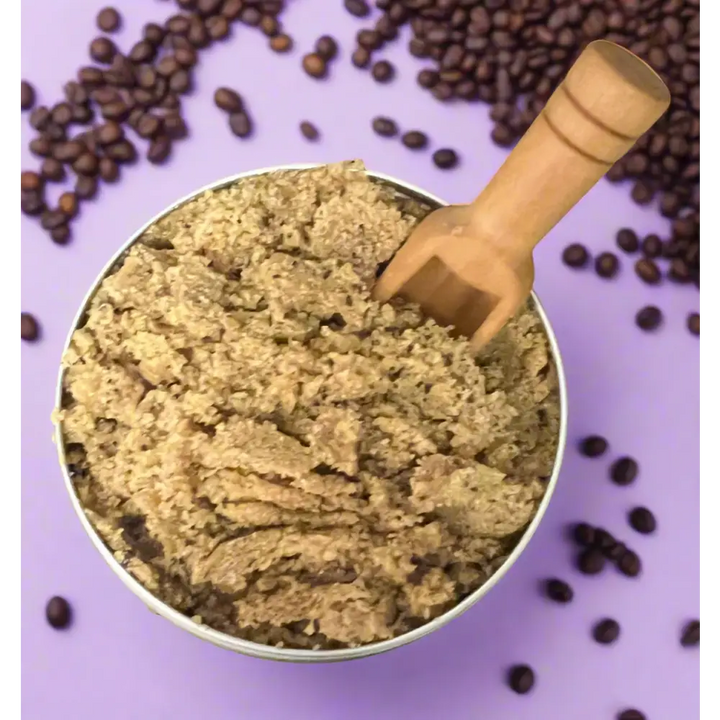 A rustic wooden scoop in a metallic bowl filled with brown sugar coffee scrub for organic coconut foot care