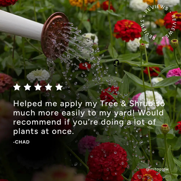 A white hose-end garden sprayer with a copper nozzle sprays water on flowers using mitogrow garden sprayer