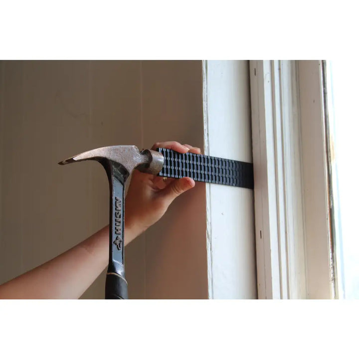 Black textured plastic glazelock shims being applied to a wall using a hammer for precise wedge spacing