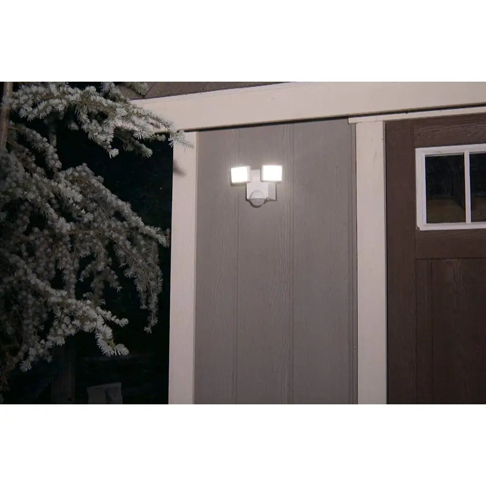White dual-head battery operated motion security flood light mounted above a gray door for outdoor use