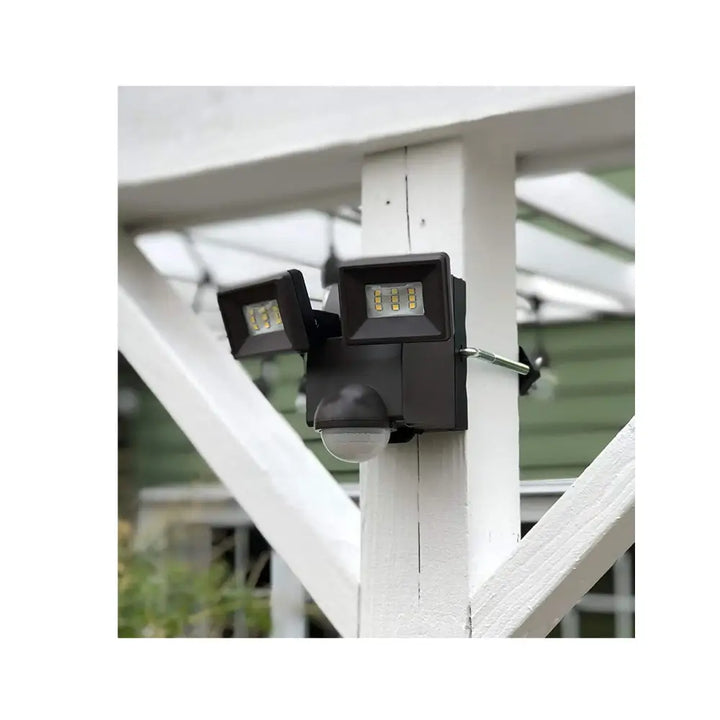 Black dual-head iq america led battery powered motion sensor flood light mounted on white wooden post eave mount