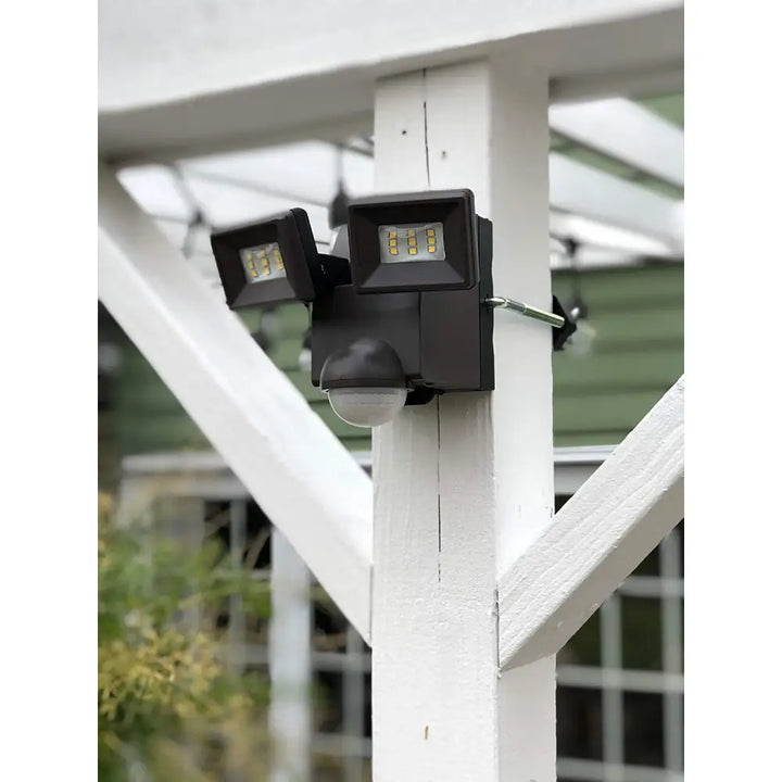 Black dual-head battery operated motion security flood light mounted on a white wooden post by IQ America