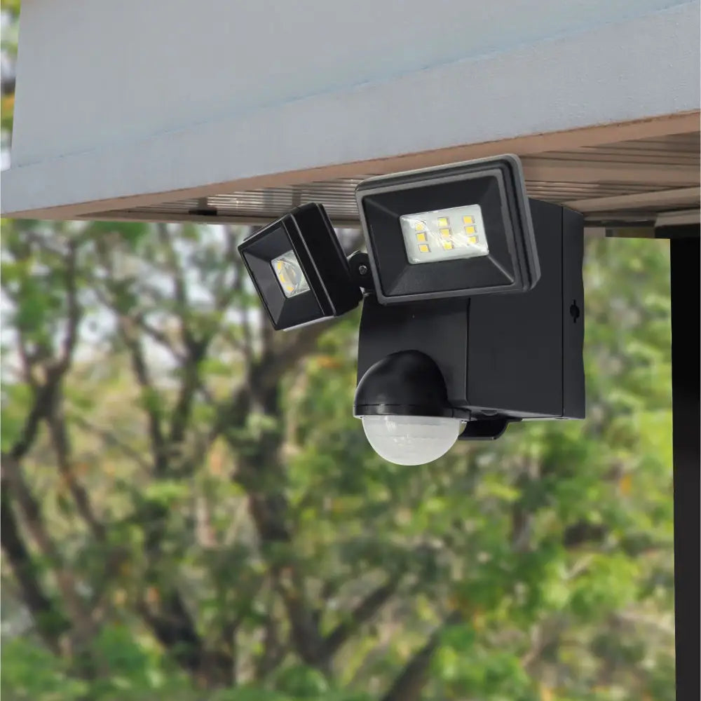 Black dual-head battery powered motion sensor flood light with frosted lens for eave mount security lighting