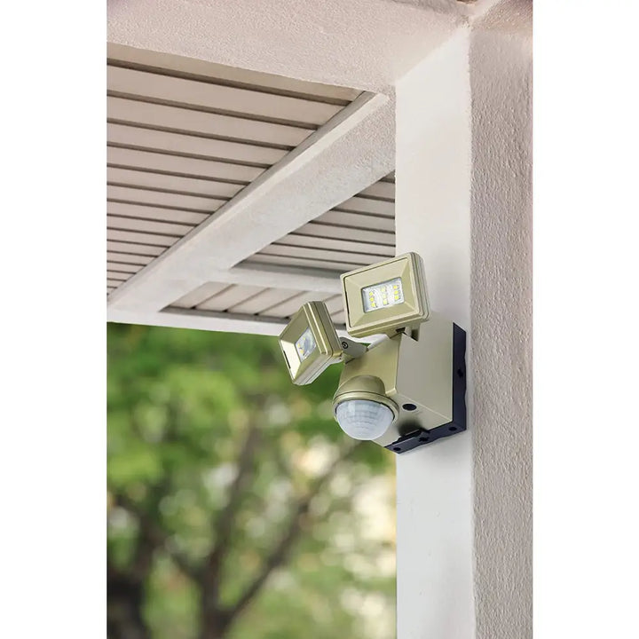 Gold-finished iq america battery powered motion sensor flood light with dual heads mounted on a wall for eave mount use