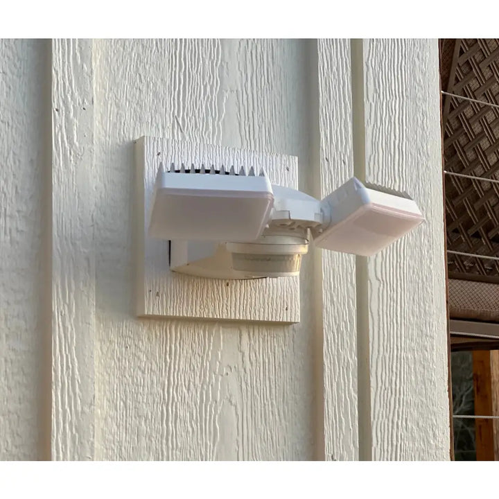 White dual-head iq america led motion sensor security flood light mounted on a textured wall for outdoor security