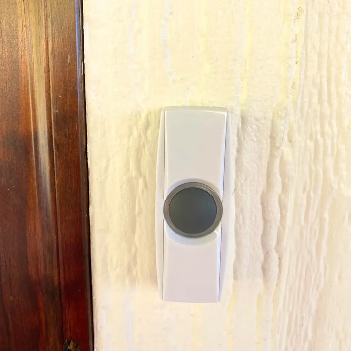 White rectangular iq america wireless portable door chime with circular gray button and dual battery powered buttons