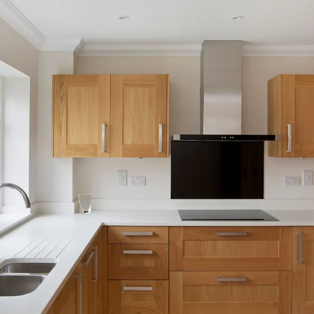 Modern kitchen with light wood cabinets, stainless steel range hood and black glass cooktop.
