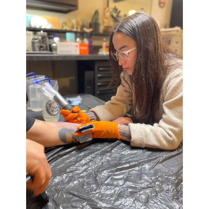 Orange natural rubber disposable latex low protein safety gloves worn by tattoo artist during session