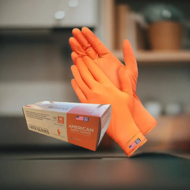 A pair of bright orange natural rubber disposable latex low protein safety gloves with american flag patch beside box