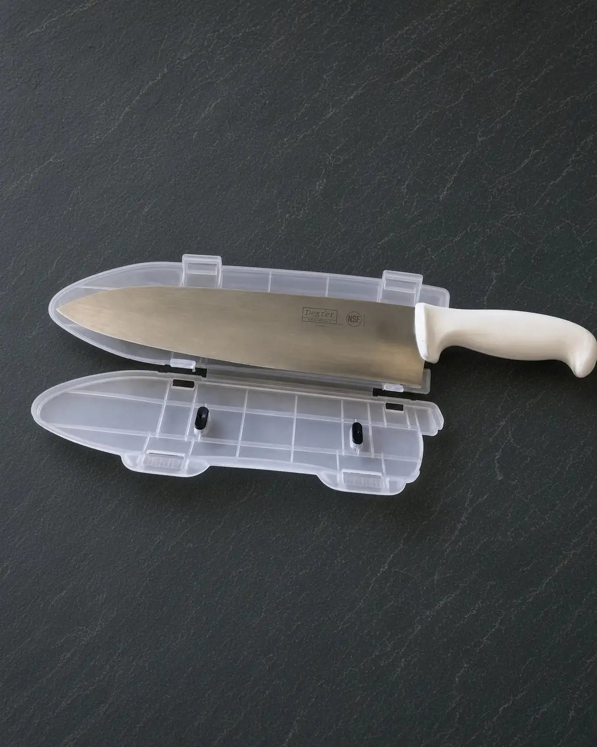 A sleek, stainless steel chef’s knife with a white handle rests in its transparent plastic sheath.