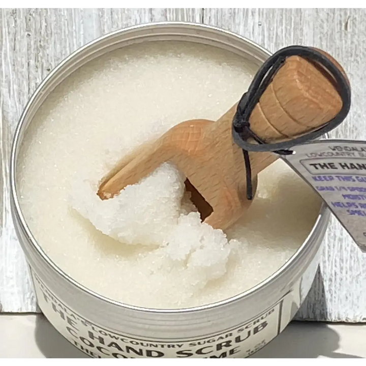 The hand scrub coconut lime white organic coconut sugar scrub in a metal tin with wooden scoop and organic coconut butter