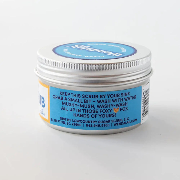 A silver metal jar of wendalas the hand scrub lemon clove with a blue and white label featuring essential oil ingredients
