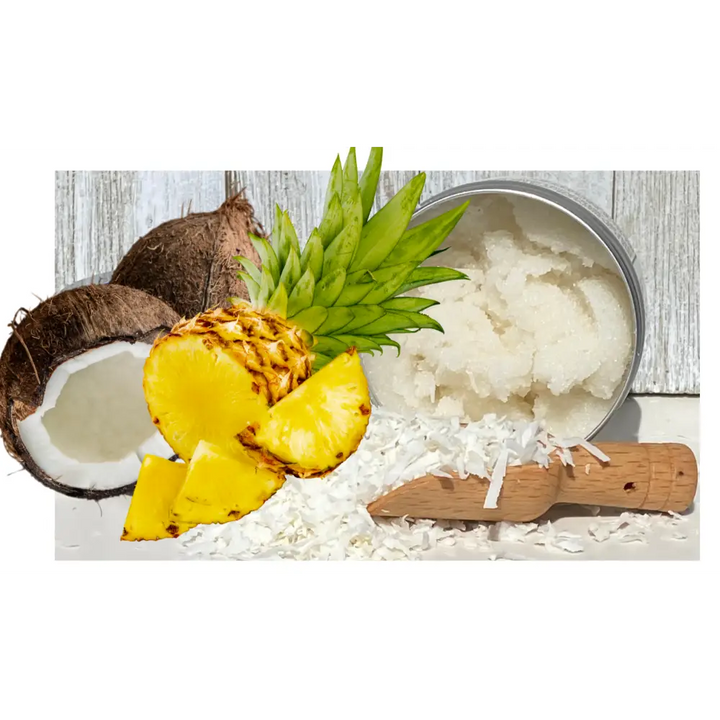 A round metal tin of white coconut oil hand scrub surrounded by pineapple slices and whole coconut for pina colada care