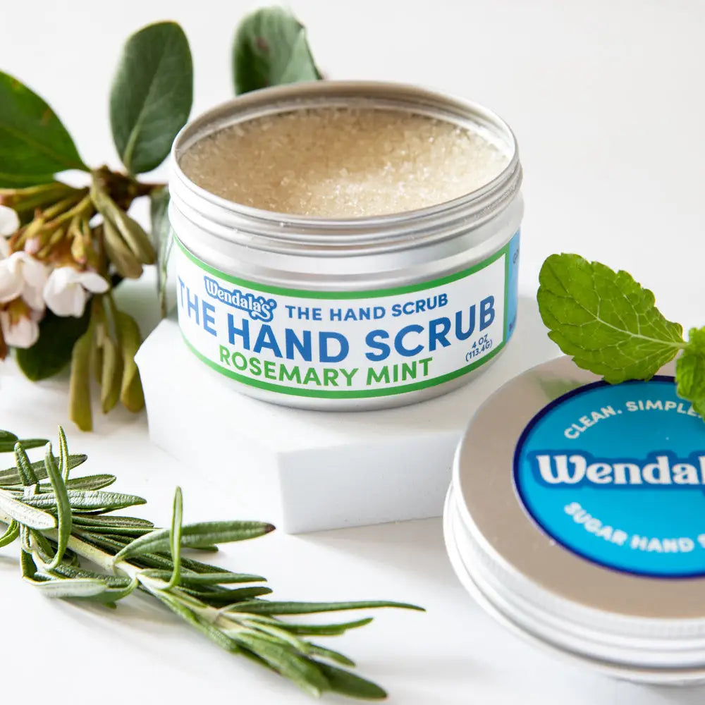 Wendys rosemary mint hand scrub in a silver jar with green and blue labels containing beige sugar exfoliant
