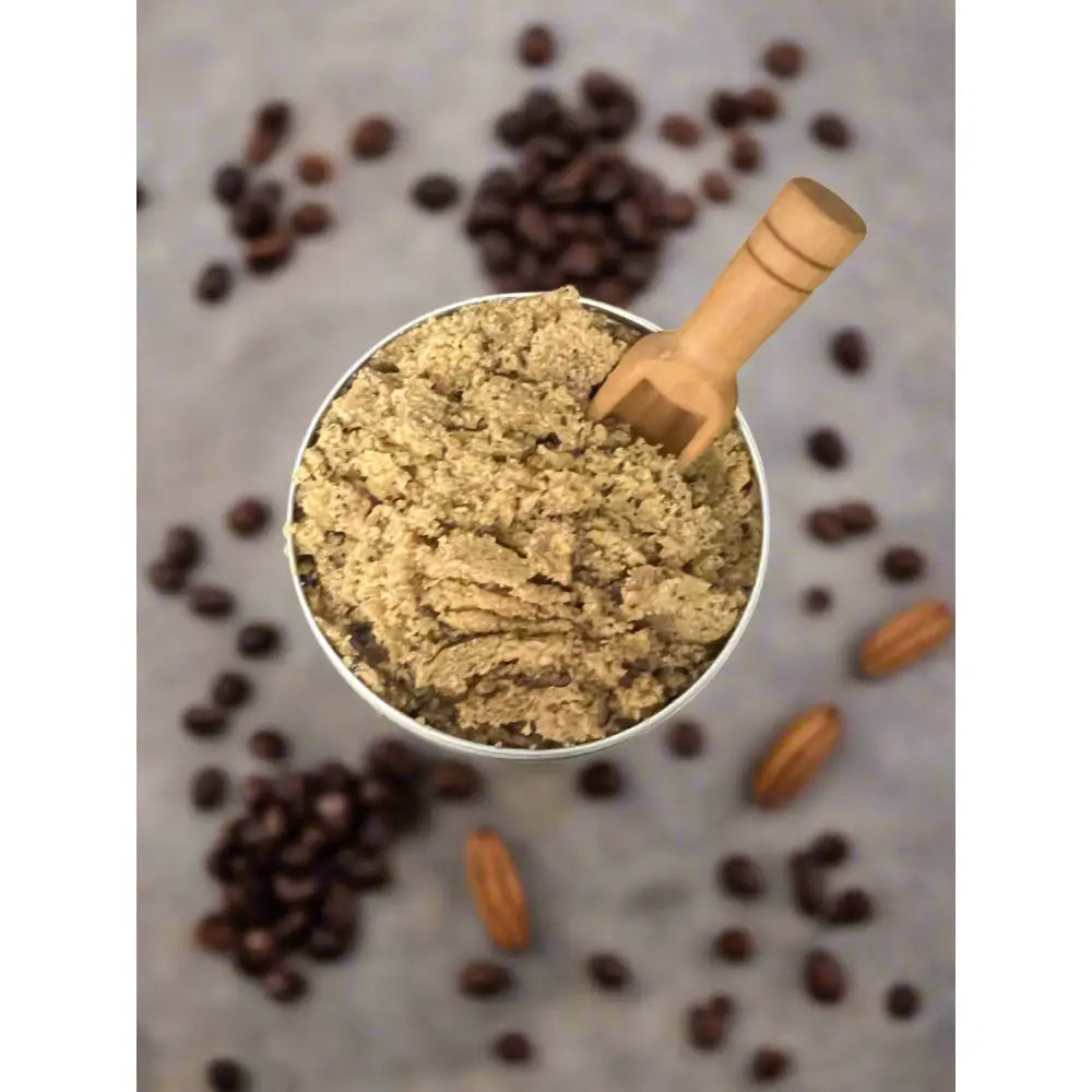 A metallic measuring cup with coarse light brown coffee scrub and wooden scoop for wendalas body scrub brown sugar vanilla organic coconut
