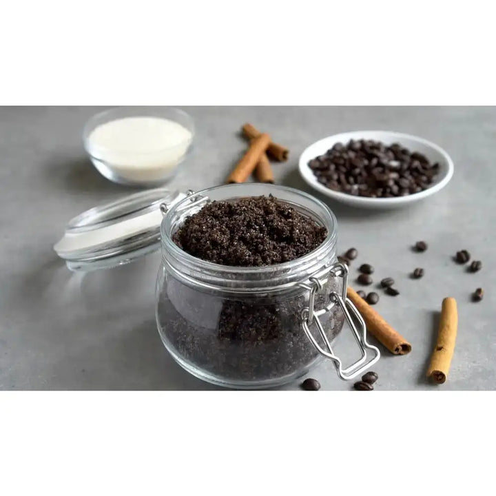 A clear glass jar with silver clasp lid filled with dark brown coffee scrubs brown sugar vanilla and organic coconut blend