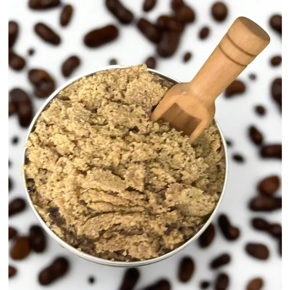 A metallic container of Wendala’s foot scrub with coarse light brown coffee scrubs and a wooden scoop to exfoliate dead skin