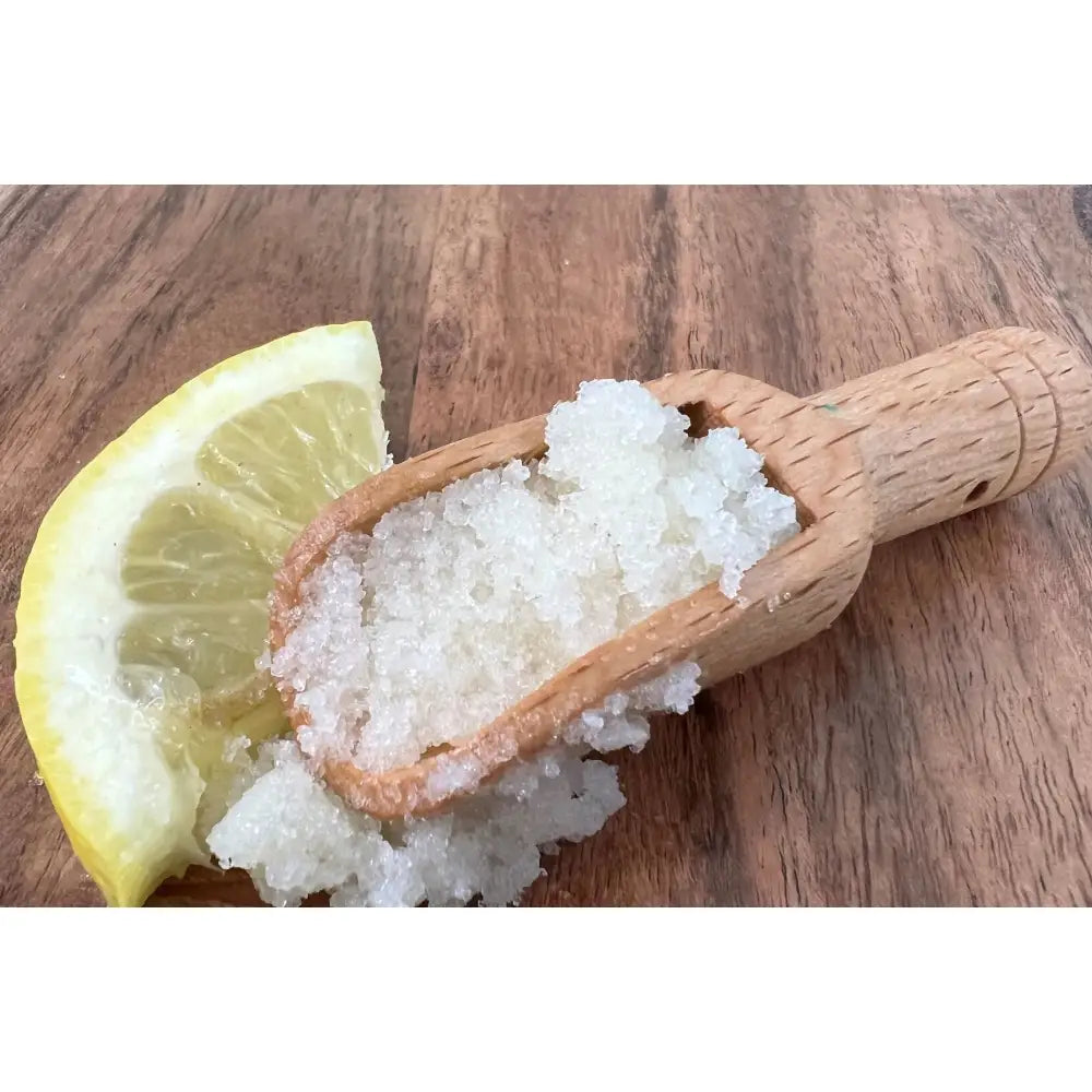 A wooden scoop filled with white crystalline sugar hand scrub with lemon clove and organic coconut on rustic wood surface