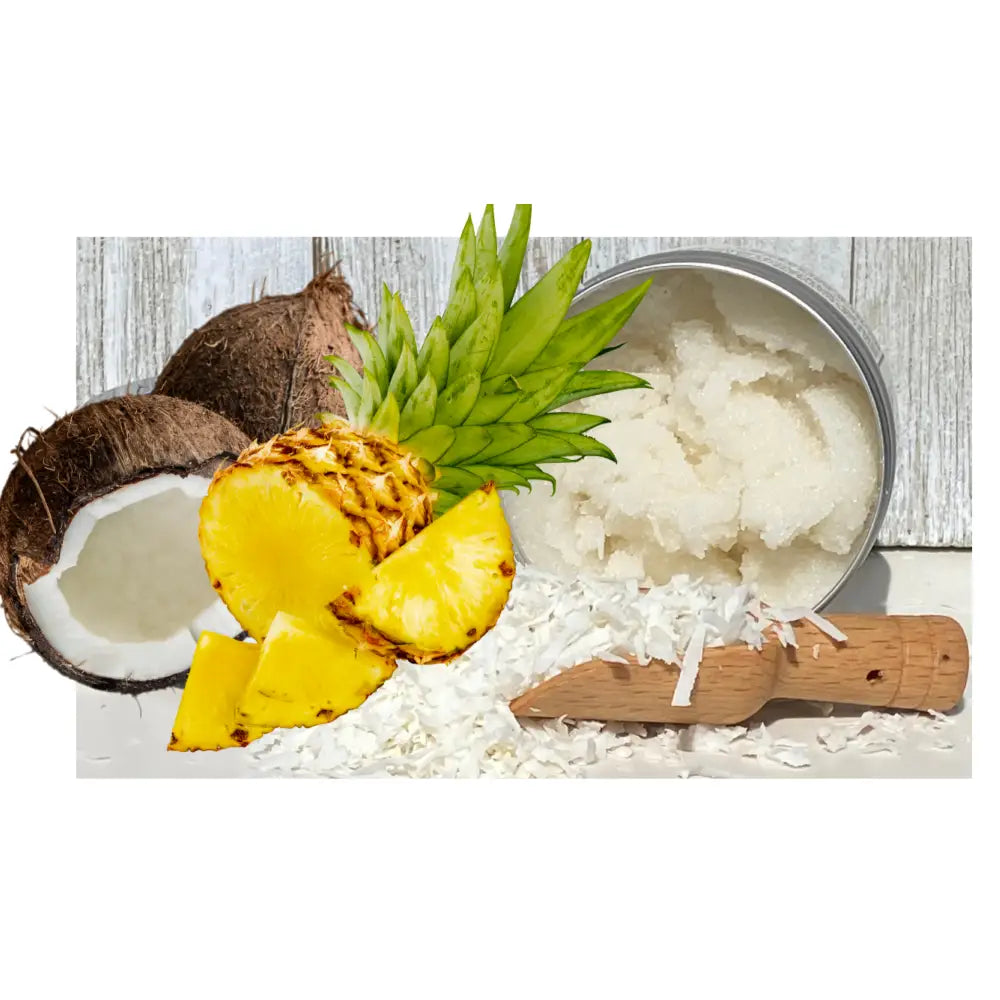 A round metal tin of white all-natural pina colada sugar hand scrub surrounded by fresh pineapple and coconut