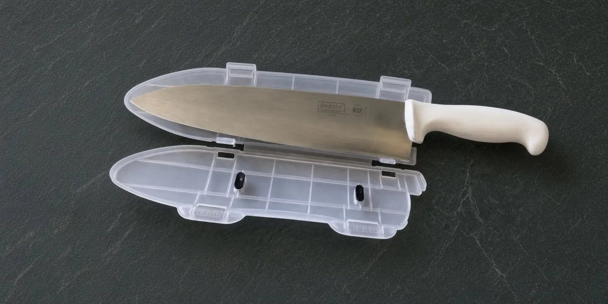 A white-handled chef’s knife with a stainless steel blade rests inside its transparent plastic sheath.